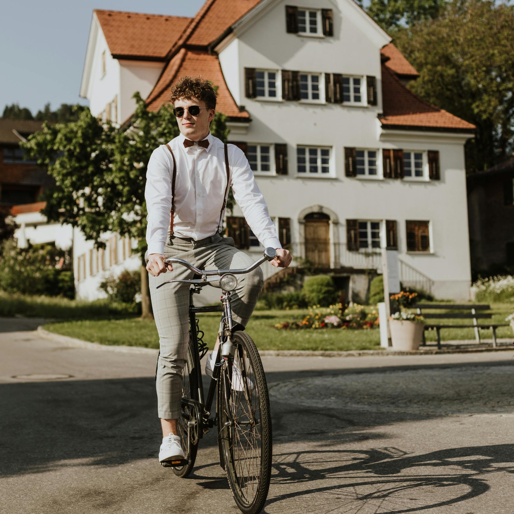 Junger Mann im urban Look trägt Hosenträger und eine Holzfliege und fährt mit einem alten Fahrrad © good matters