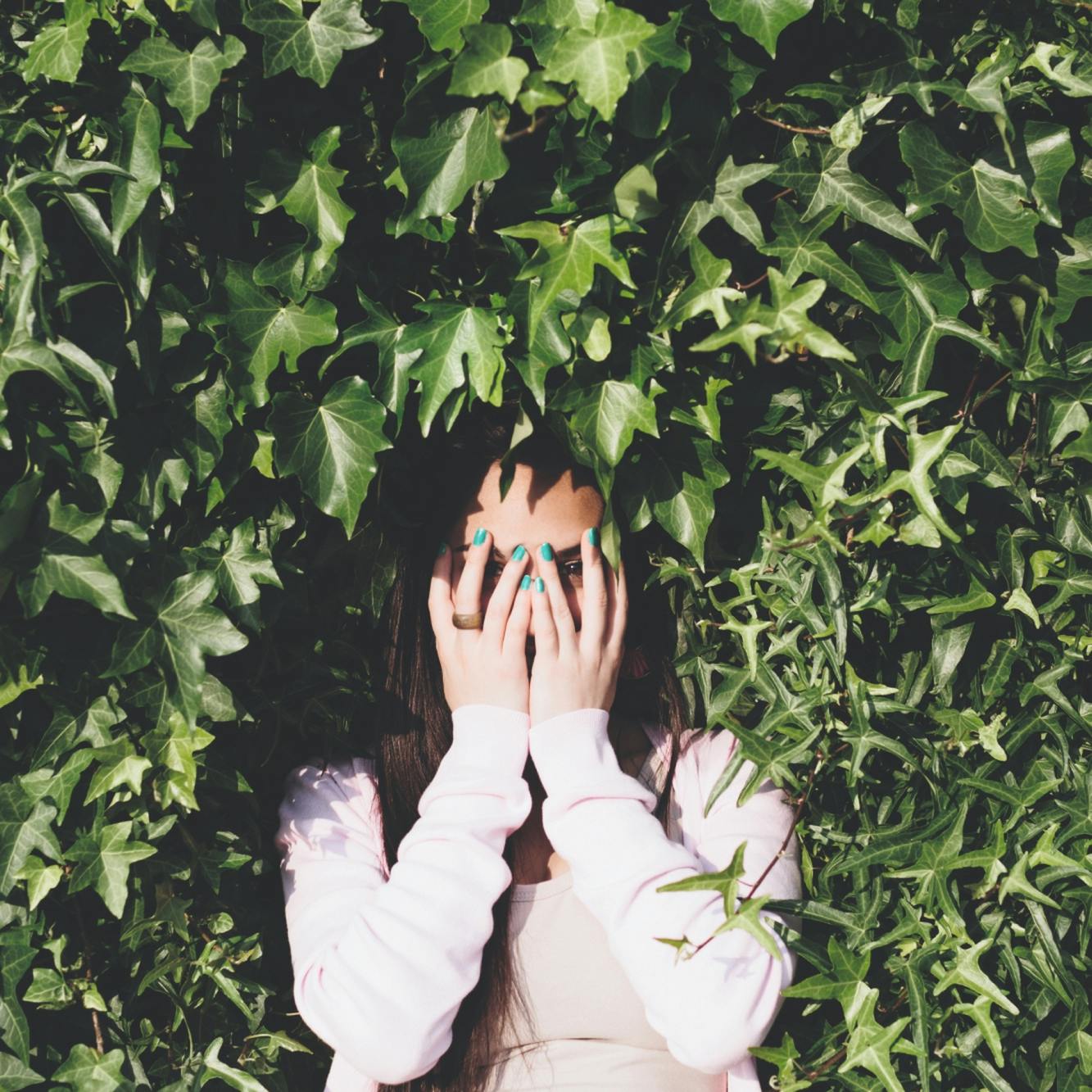 Fröhliches junges Mädchen steht in einer grünen Hecke und hat ihre Hände vor dem Gesicht © gobiq